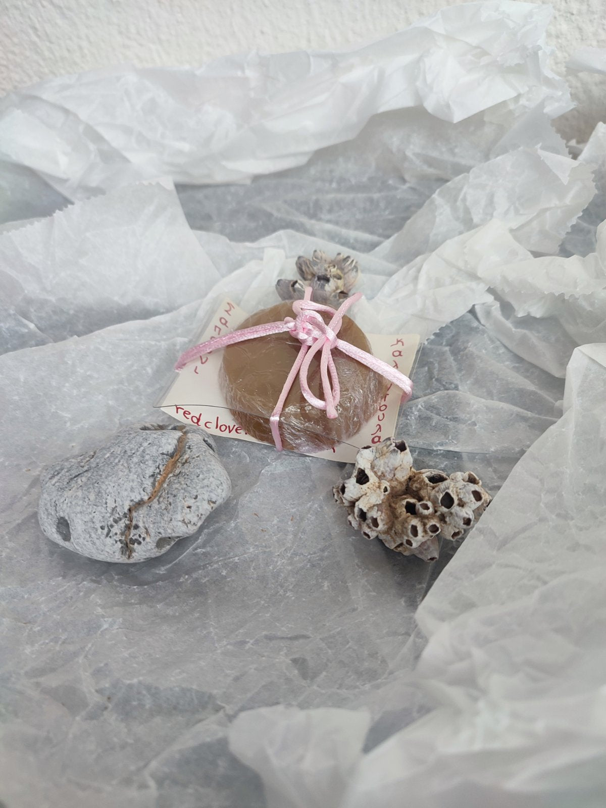 Handcrafted natural soap bar with pink ribbon displayed with sea stones and dried botanicals, gentle skincare.